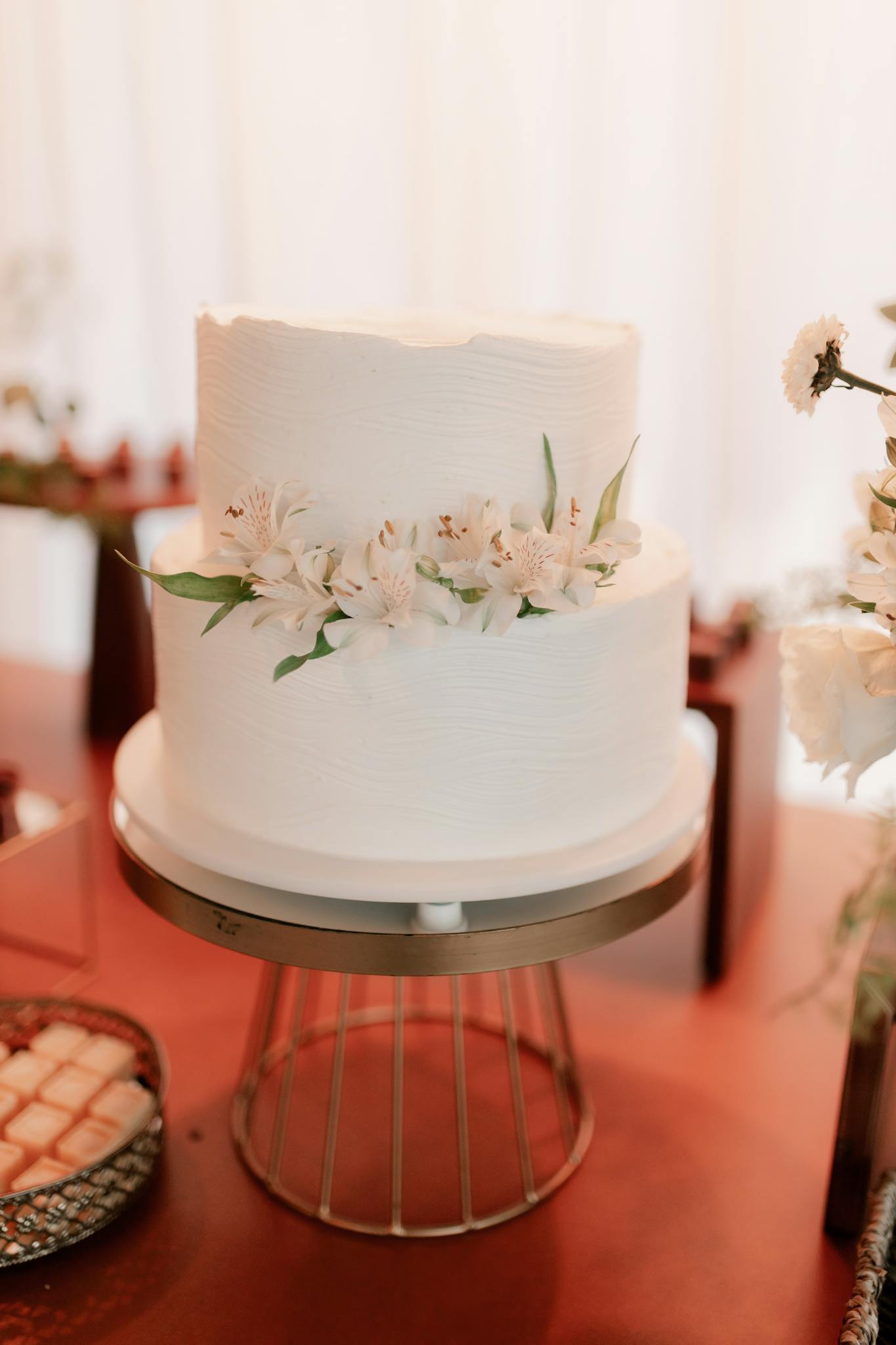 Two-tier white wedding cake adorned with fresh flowers on a stylish stand.